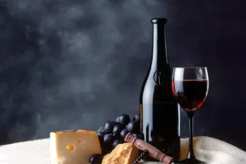 Botella, copa de vino tinto, uvas y queso.