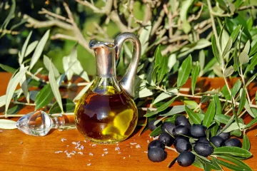 Una aceitera con aceite de oliva al lado de unas aceitunas negras.