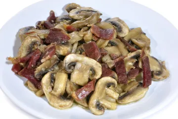 Champiñones salteados con jamón serrano en plato blanco.