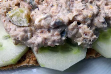 Primer plano de pasta de sardinas sobre rodajas de pepino en una galleta salada.