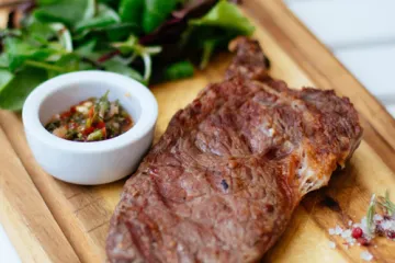 Filete a la plancha sobre tabla de madera con salsa y rúcula.