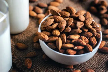 Almendras en un bol, vaso y botella con leche de almendras.