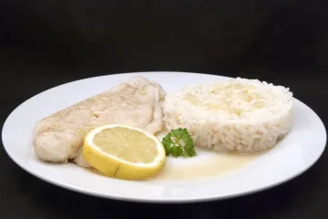 Pescado escalfado con arroz blanco y una rodaja de limón.