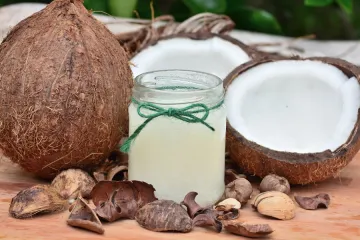 Un coco entero, aceite de coco en un vaso de vidrio y un coco partido por la mitad.