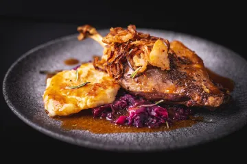 Una pieza de ganso asado servida con su guarnición y su salsa.