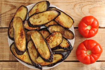 Berenjenas fritas en un plato junto a dos tomates.
