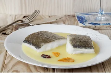 Dos trozos de bacalao al pil-pil con su salsa en un plato.