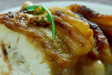 Detalle de bacalao hecho en el horno con tocino ahumado.