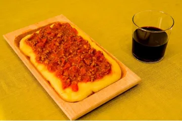 Una fuente de madera con polenta con salsa de carne y un vaso de vino tinto.