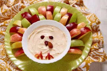 Un cuenco con crema de queso al caramelo, decorado como un pollito, rodeado de trozos de manzana.