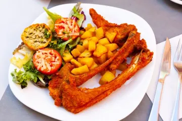 Chuletas de cordero empanadas con patatas fritas y ensalada.
