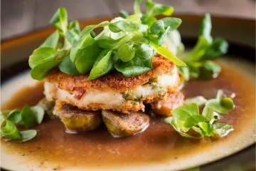 Un plato con tortitas de patata sobre coles de bruselas y salsa, decoradas con canónigos.