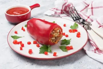 Un plato con un pimiento parecido a los pimientos de piquillo relleno decorado con pimiento picado.