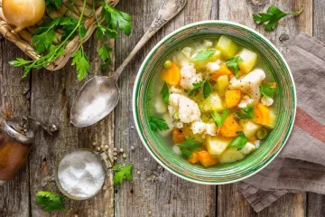 Un taz'on con sopa de verduras sobre madera.