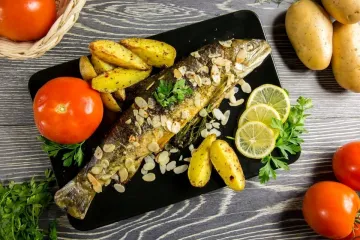 Trucha con almendras acompañada de patatas, rodajas de limón y un tomate.