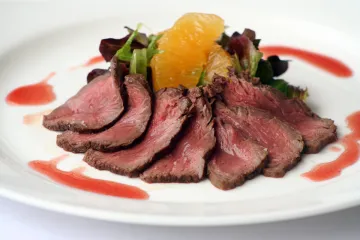 Canguro a la plancha fileteado fino con salsa de frambuesa y ensalada de naranja.