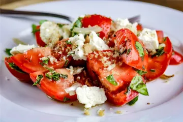 Ensalada de tomate y queso con pangrattato en un plato blanco.