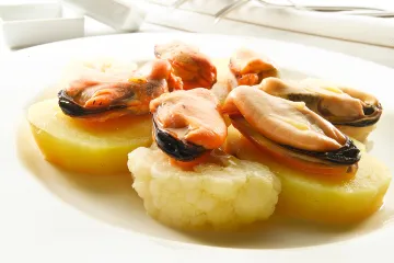 Mejillones con patatas en un plato, las patatas peladas, los mejillones sin valvas.