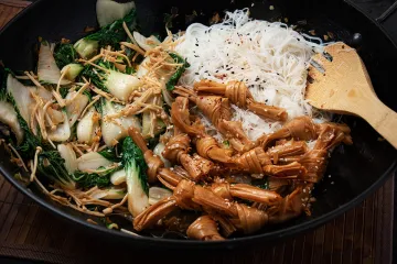 Bok choi salteado con enokis y nudos de tofu servido con fideos finos de arroz.