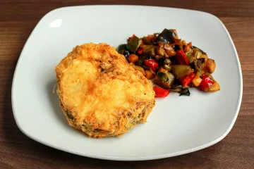 Una rodaja de merluza rebozada a la romana acompañada de verduras braseadas.