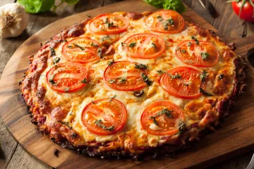 Pizza de queso y rodajas de tomate con base de coliflor.