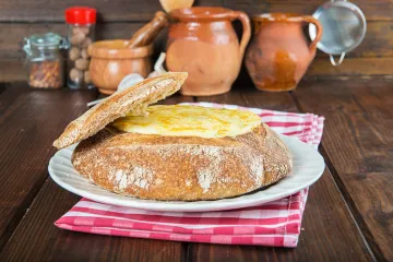 Besamel cremosa de bacalao gratinada con queso rallado en una hogaza de pan vaciada.