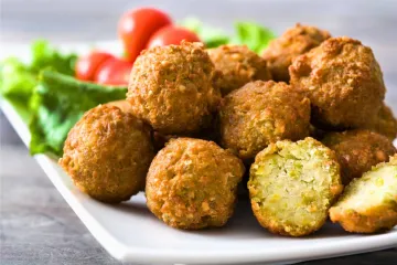Un plato con varios falafel, uno de ellos cortado por la mitad y mostrando el interior.