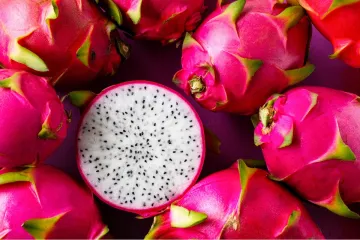 Una pitaya cortada por la mitad transversalmente en medio de varias pitayas enteras.