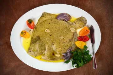 Un plato con un rodaballo escalfado cubierto de salsa gallega, acompañado de pimientitos.