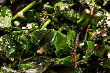 Primer plano de acelgas rehogadas con ajo y almendras picadas.