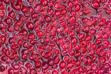 Vista superior de cerezas de color rojo vibrante en un jarabe espeso y brillante, con las cerezas empaquetadas juntas y algunas ligeramente machacadas, creando una superficie rica y texturizada.