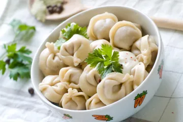 Un cuenco de pelmeni ruso con guarnición de eneldo fresco.