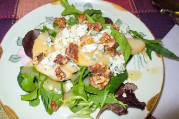 Un plato con ensalada de hojas variadas, queso azul, nueces y pera.