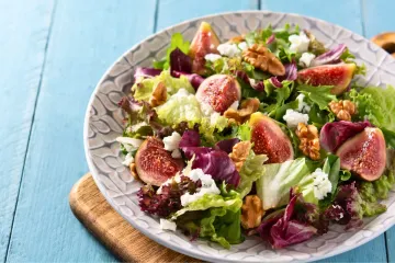 Un plato con ensalada de hojas variadas, queso de cabra e higos.