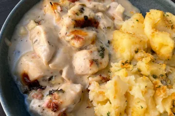 Un plato de pollo a la bretona con jamón desmenuzado acompañado con puré de patata al queso.