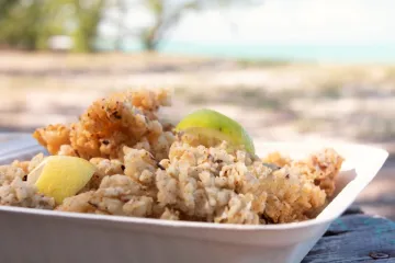 Fritos de caracol, cracked conch, con cuartos de lima en un contenedor rectangular