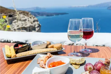 Comida y vino griegos en una terraza con vistas a un mar Mediterráneo de color azul brillante.