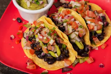 Tres tacos de alubias negras acompañados de salsa.