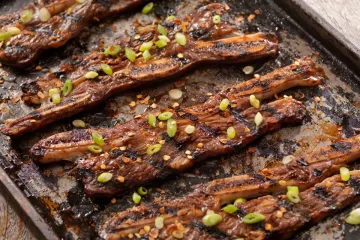 Costillas adobadas y cocinadas sobre la barbacoa al estilo coreano sobre una tabla de madera.