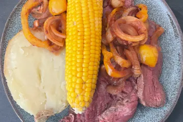 Lonchas de filete de vaca a la barbacoa con una salsa hecha del adobo, acompañado de maíz y patata asados.