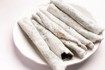 Un plato de loza blanca con rollitos de sésamo conocidos como til pita.