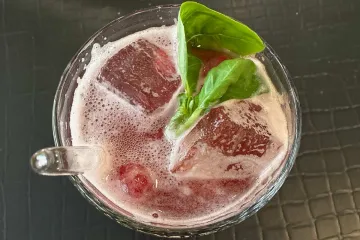 Un vaso con limonada de frambuesa e hibisco alemana, con hielo y hojas de albahaca.