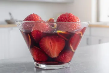 Un recipiente con fresas al vino tinto con piel de naranja finamente cortada.