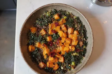Cuenco de calabaza asada, lentejas y col reizada, con tomates secos, visto desde arriba sobre una encimera de mármol.