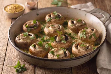 Champiñones asados con mostaza y perejil fresco en una fuente de horno esmaltada sobre una mesa de madera.