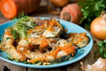 Rodajas de pescado en escabeche con zanahoria y cebolla, servidas en un plato azul y decoradas con eneldo fresco.