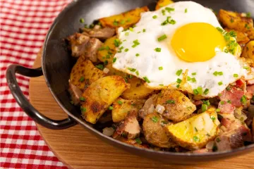 Gröstl tirolés en una sartén de hierro: patatas en rodajas doradas con tiras de carne asada y cebolla, coronado con un huevo frito.