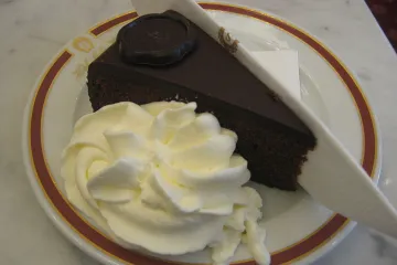 Un trozo de sachertorte en un plato, acompañado de nata montada.