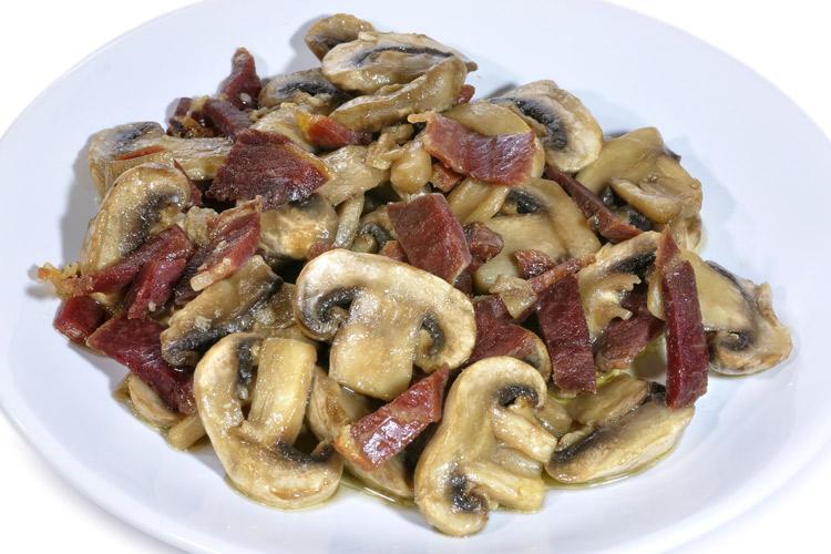 Champiñones salteados con jamón serrano en plato blanco.
