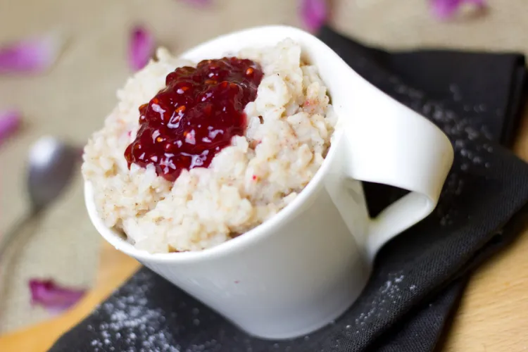 Budín de arroz servido en una taza blanca y coronado con mermelada de frutos rojos.